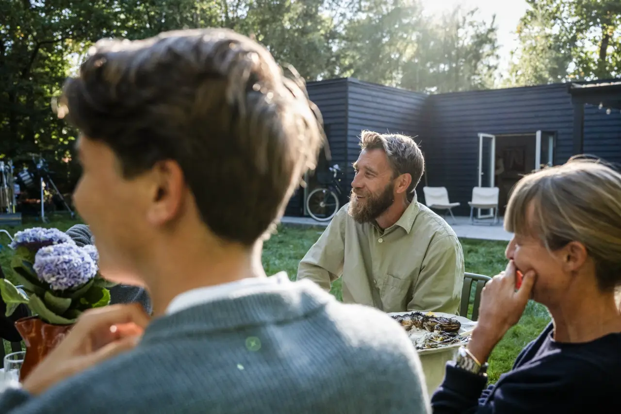 People preparing fresh ingredients together on a table under a covered terrace surrounded by greenery.