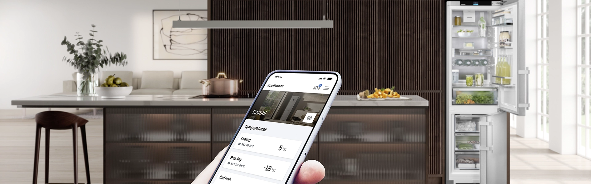 Modern kitchen with an open fridge on the right; in the foreground, a hand is holding a smartphone displaying the SmartDevice app for controlling the fridge.