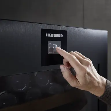 Hand stellt am digitalen Display die Luftfeuchtigkeit im Weinkühlschrank eines Vinidor-Modells auf 70 % ein