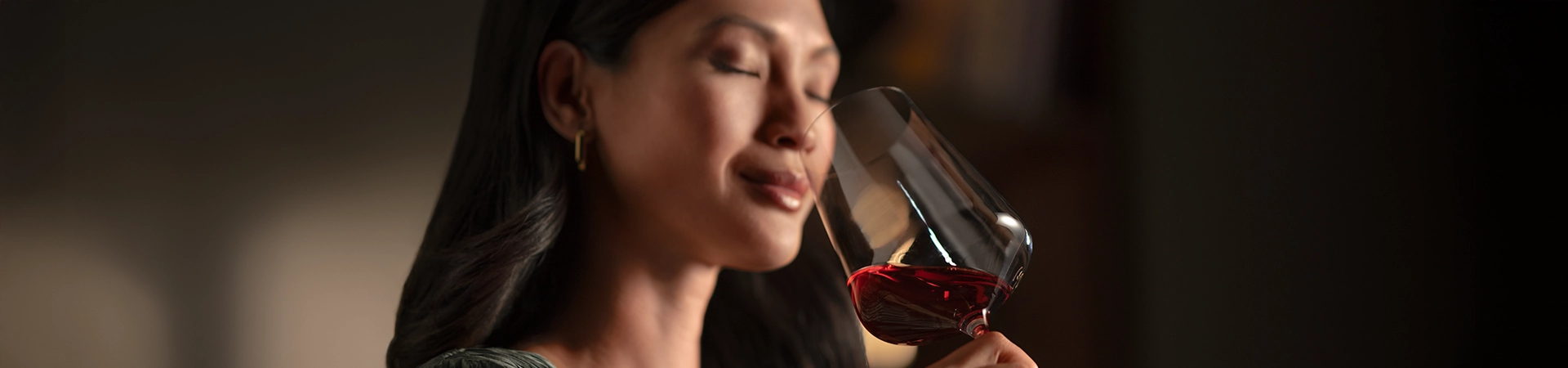 Person genießt ein Glas Rotwein und riecht mit geschlossenen Augen daran vor einem Weinkühlschrank.
