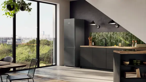 A freestanding fridge in  DarkGrey in a modern kitchen unit and a large window with a view of the greenery