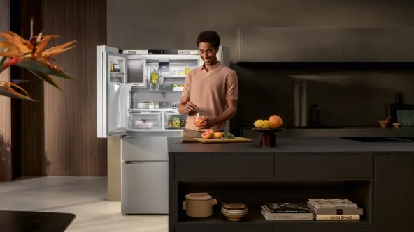 A man prepares a drink with grapefruit in front of an open French Door fridge set in a modern and dark kitchen