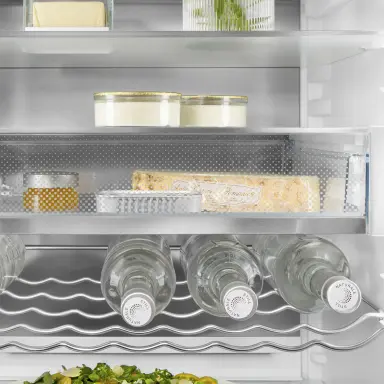 Drei Wasserflaschen liegen waagrecht im Metall-Flaschenbord im unteren Bereich eines Kühlschranks.