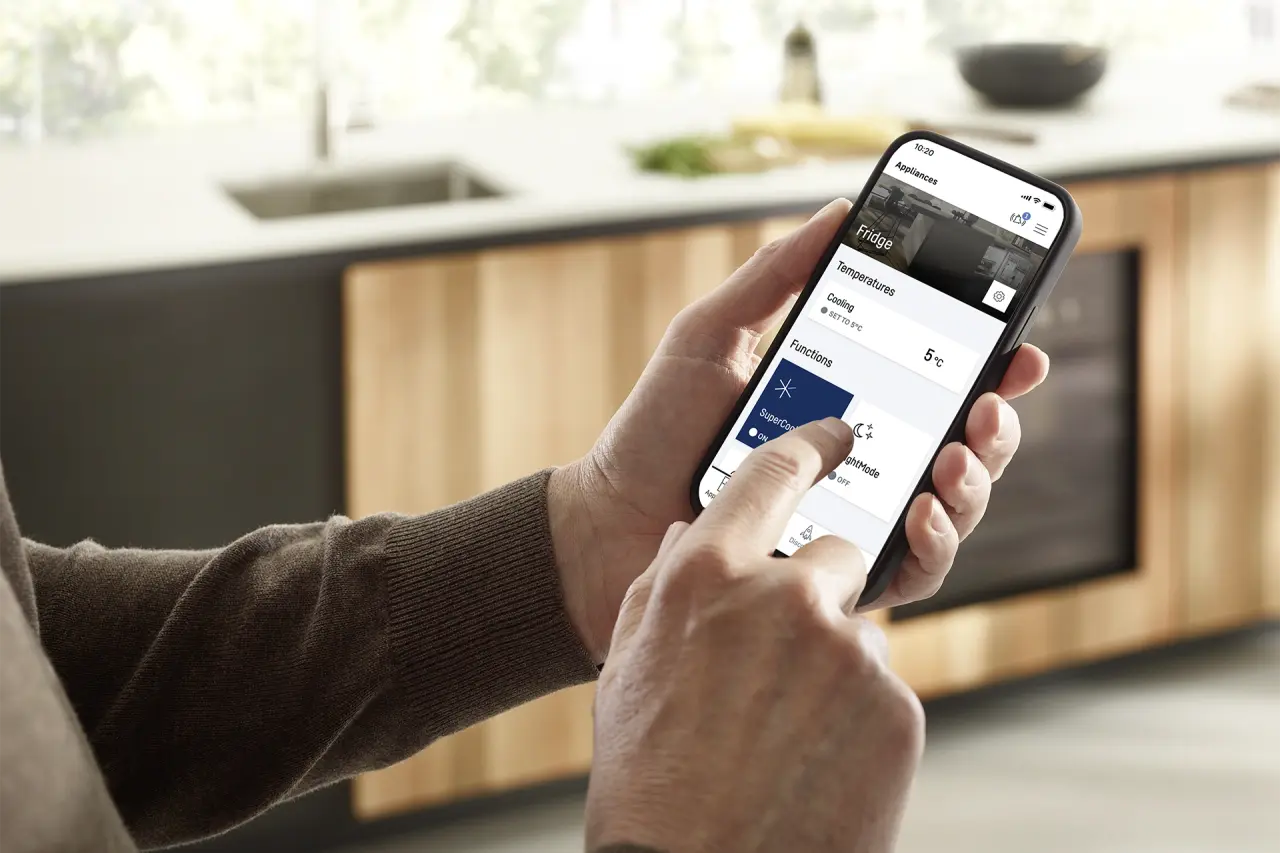 Person hält Smartphone, tippt auf Display, unscharf im Hintergrund Outdoor-Küche mit Kühlschrank