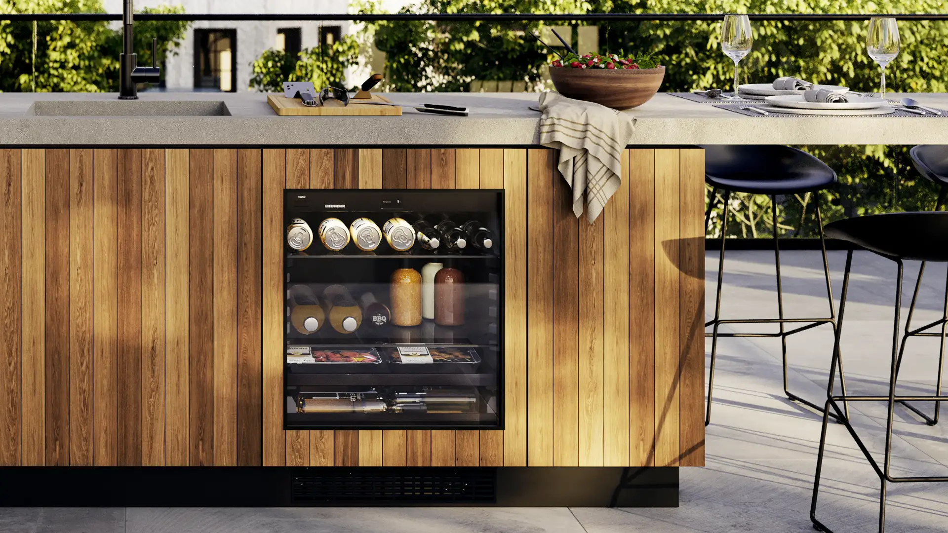 In Outdoor-Küche eingebauter Outdoor-Kühlschrank mit Holzdekor, gefüllt mit Getränken und verpackten Snacks.