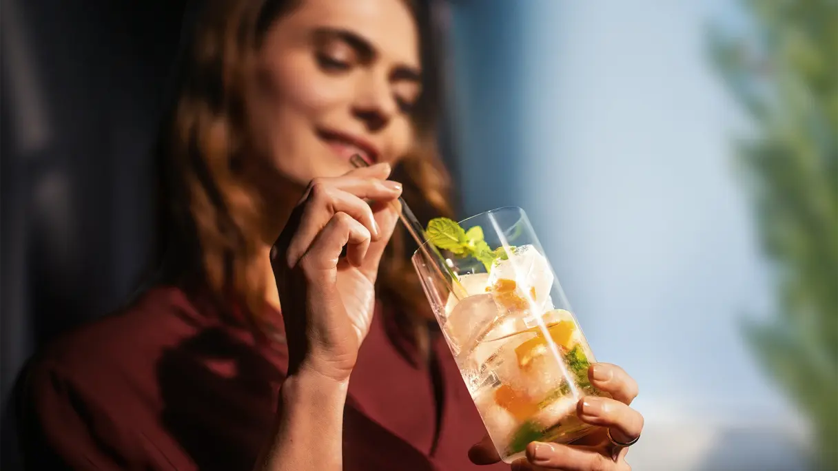 Person hält Drink mit Zitrus und Minze in der Hand, unscharfer Hintergrund mit Natur