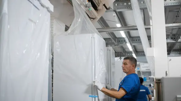 A man is focused on packaging a fridge with transparent foil, skillfully wrapping the appliance