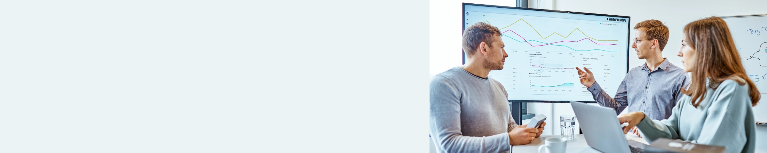 A diverse group of professionals engaged in a lively discussion, gathered around a large screen displaying important information. One participant is using a laptop to share insights, while others contribute ideas and feedback.