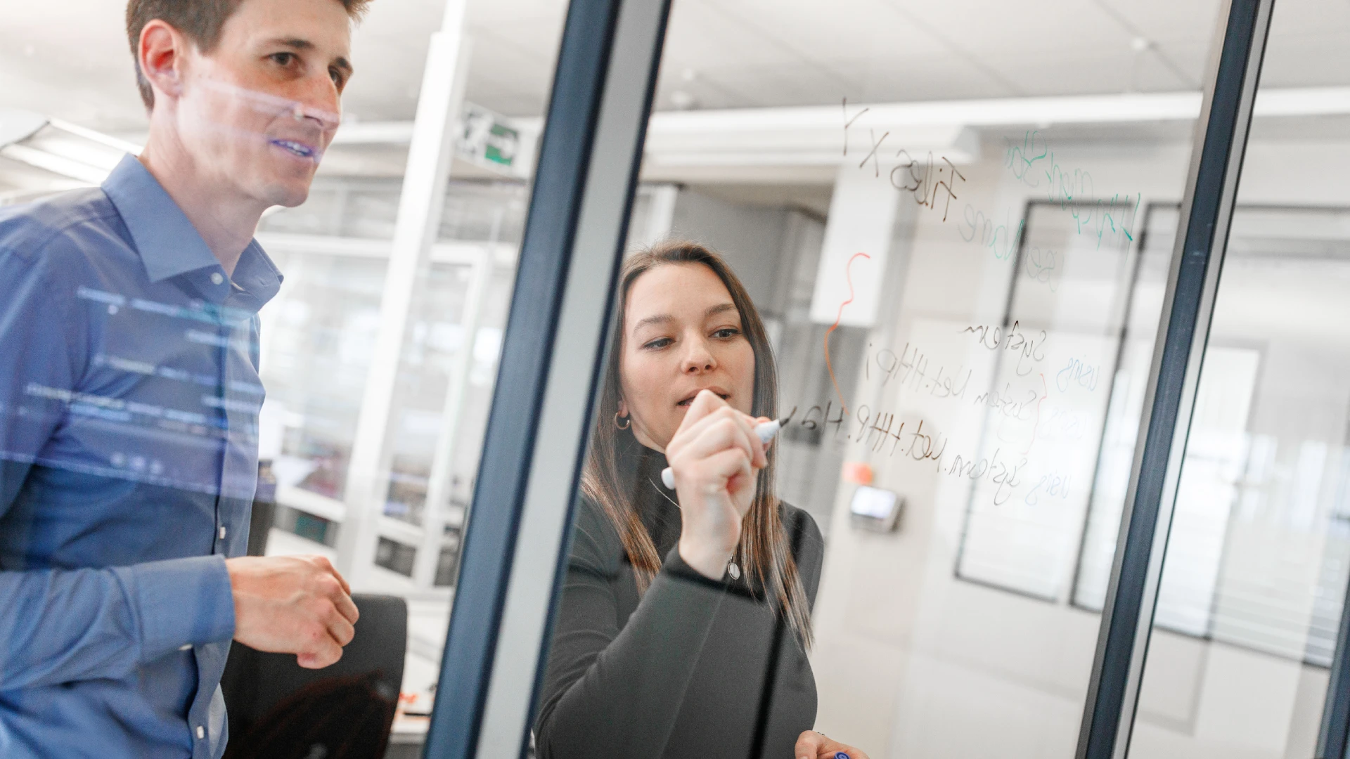 Two persons collecting and discussing ideas and writing them on a glass board.