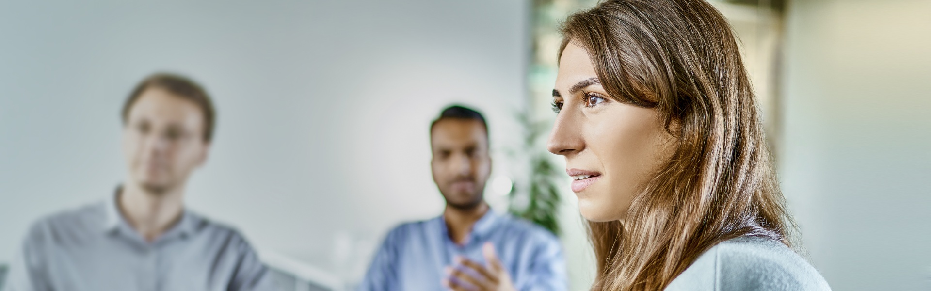 A group of professionals is engaged in a lively discussion in an office setting with a woman is in focus, looking to the left