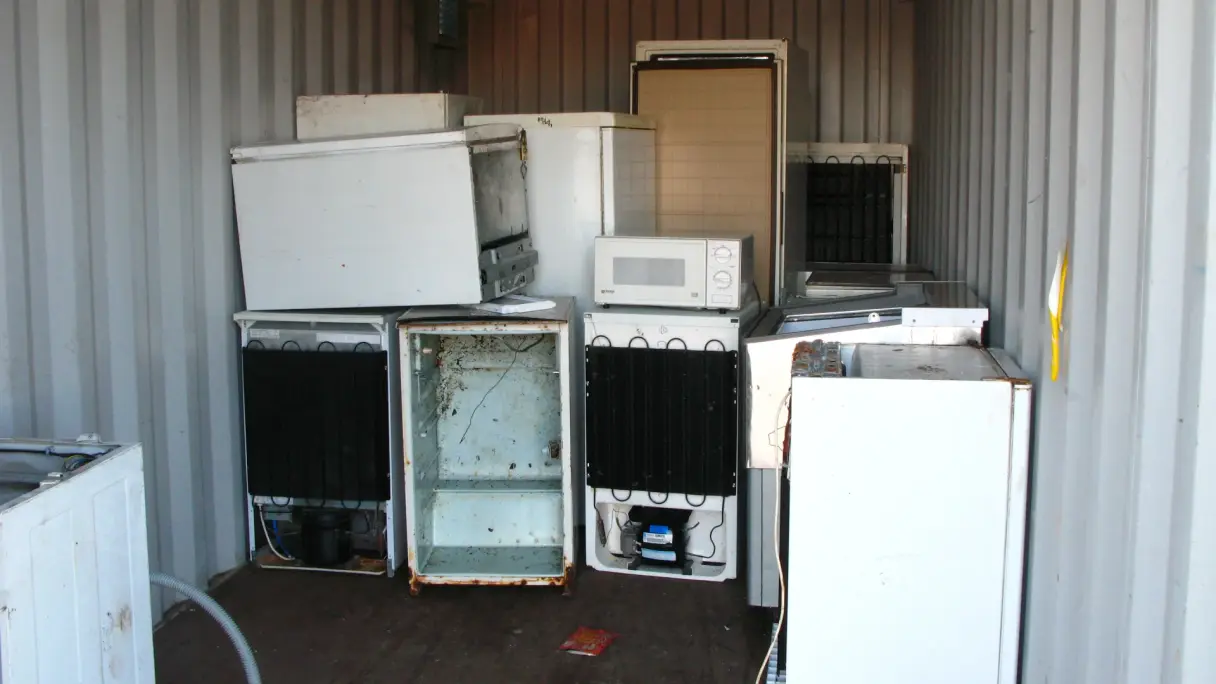 A container filled with old fridges and various household appliances, emphasizing the importance of recycling. The scene highlights the collection of discarded items, showcasing the need for responsible disposal and environmental sustainability. 