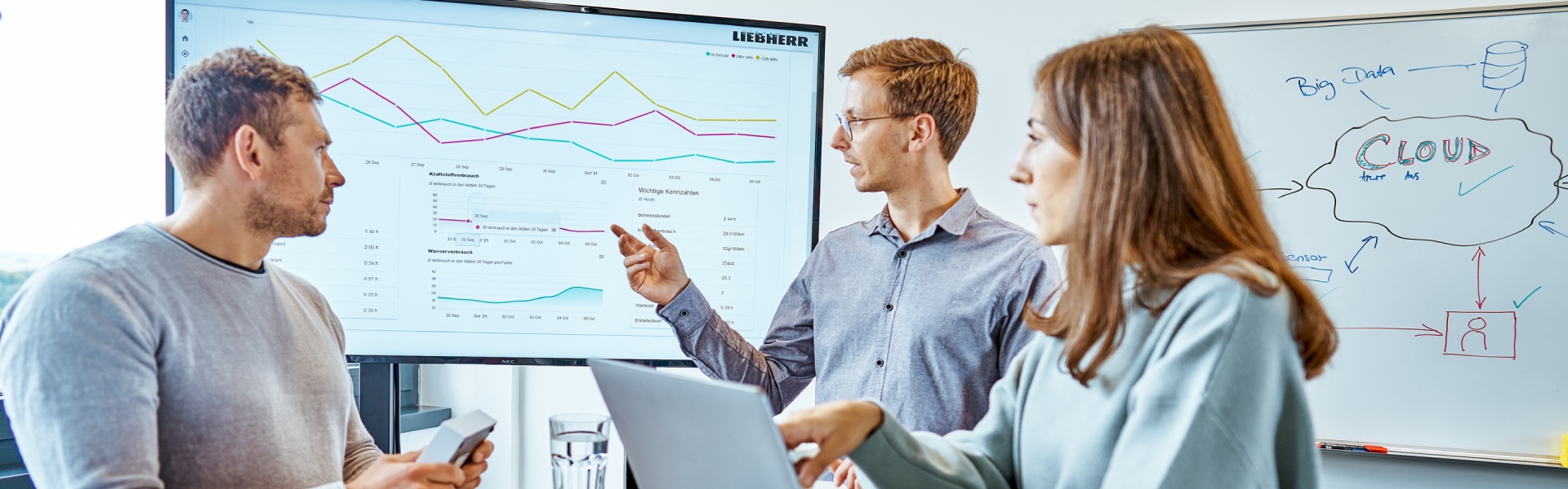 A diverse group of professionals engaged in a lively discussion, gathered around a large screen displaying important information