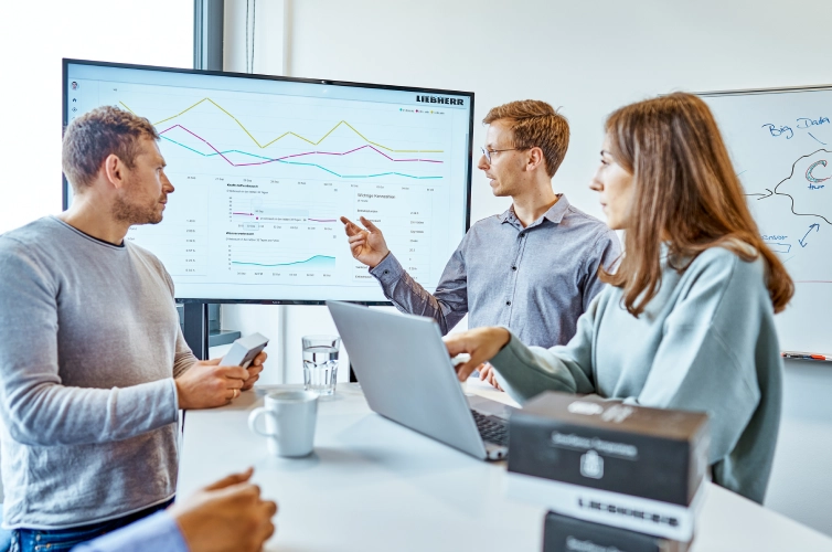 A diverse group of professionals engaged in a lively discussion, gathered around a large screen displaying important information