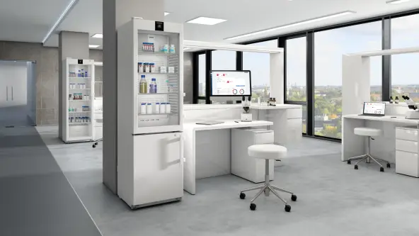 Modern laboratory workplace featuring a desk with a monitor displaying statistics. White furniture and laboratory fridges with glass doors are visible, conltaining medication and samples.