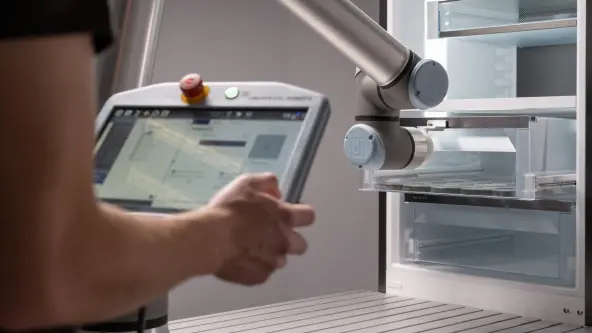 A person is holding a tablet as a robotic arm conducts quality testing on a drawer.