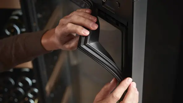 Two hands are carefully replacing the door seal of a fridge door.