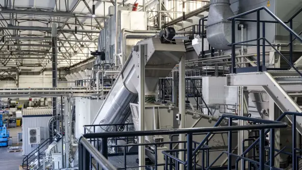 Inside a recycling facility, an industrial hall features a slide for transporting materials and scaffolding for structural support.