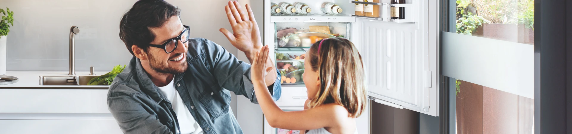 Man and child high fiving in kitchen in front of an open fridge.