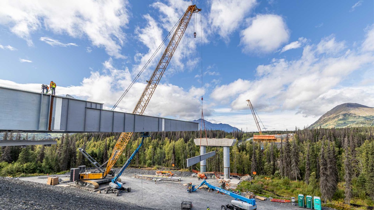 A Liebherr LR 1300.1 SX crawler crane helps place steel girder sections for the Juneau Creek Bridge near Cooper Landing, Alaska, as the span is assembled and launched across the canyon.