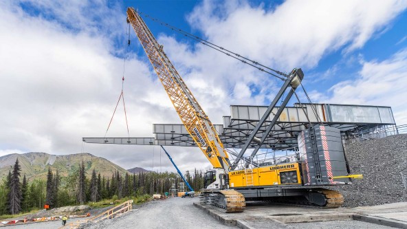 At a remote Kenai Peninsula jobsite near Cooper Landing, two Liebherr LR 1300.1 SX crawler cranes support construction of the 951‑foot Juneau Creek Bridge, lifting steel girder sections as the bridge is launched across the Juneau Creek canyon.