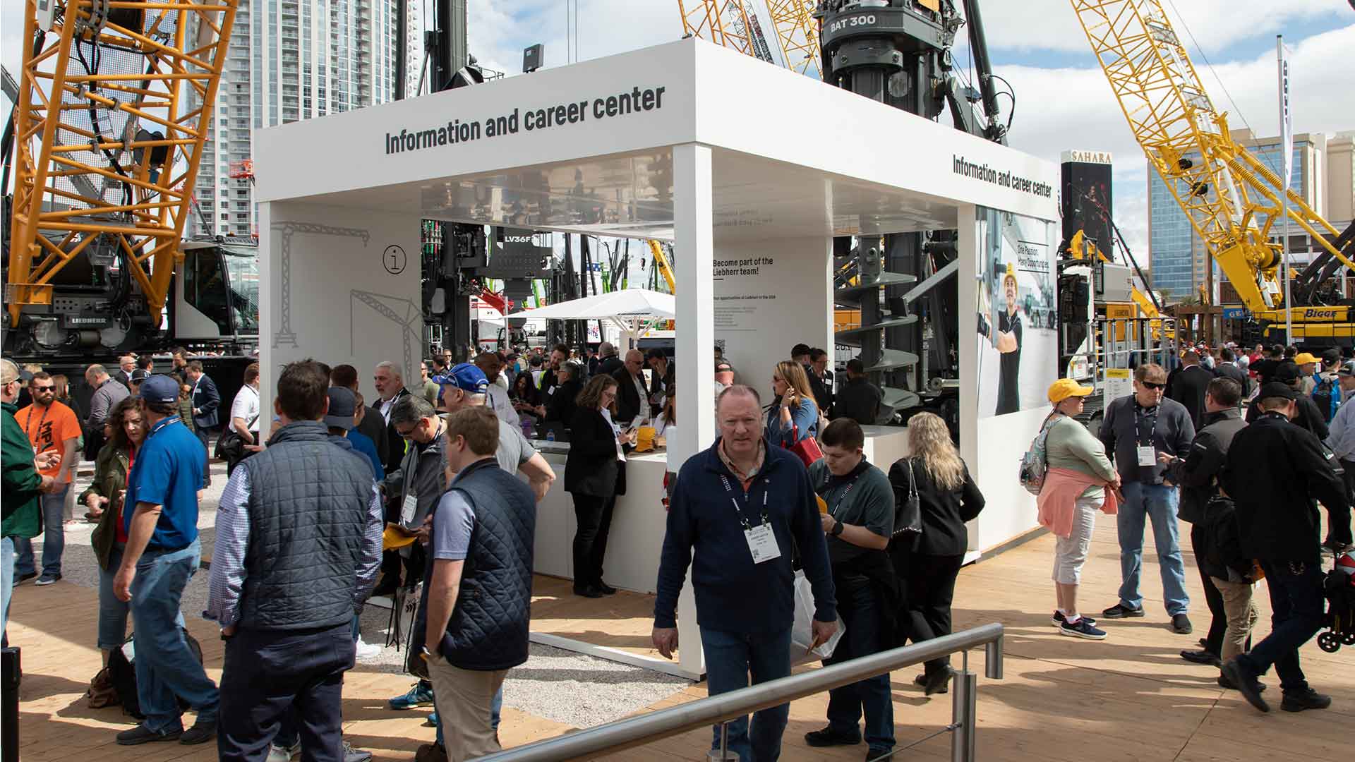 Crowds visiting the Liebherr Information and Career Center at CONEXPO 2023 in Las Vegas, surrounded by heavy equipment displays and cranes.