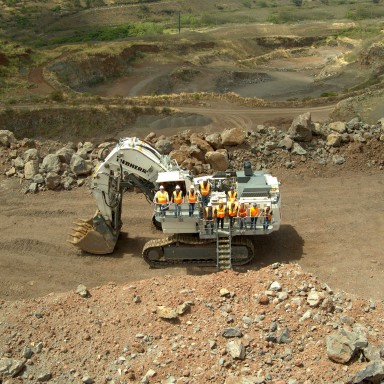 Hawaii Cement team in yellow safety vests standing on a white Liebherr R 9150 mining excavator at the Halawa Valley Quarry.