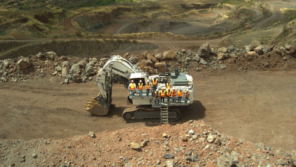 Hawaii Cement team in yellow safety vests standing on a white Liebherr R 9150 mining excavator at the Halawa Valley Quarry.