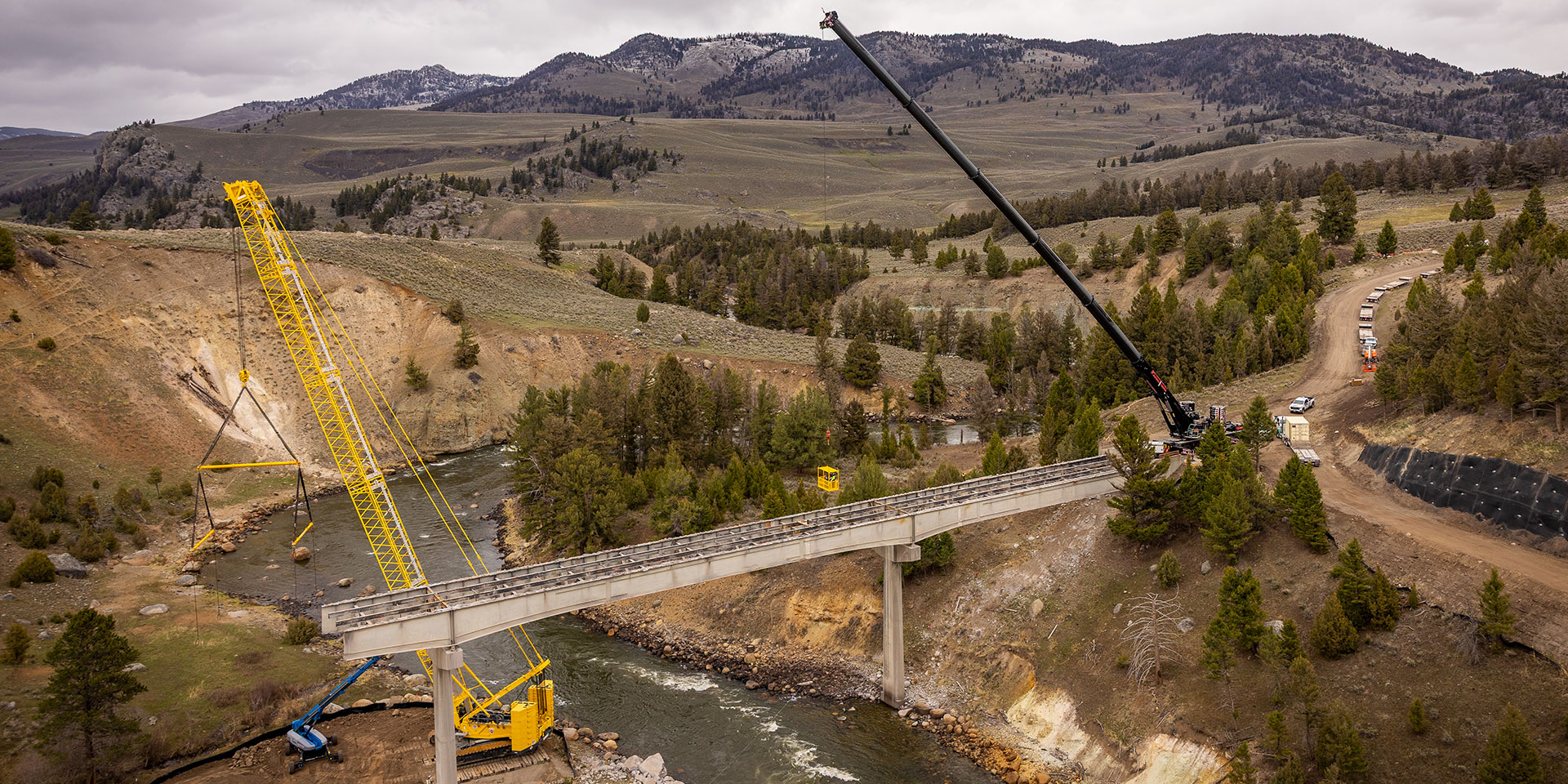 Liebherr mobile cranes lift bridge components in a rugged mountain work zone, demonstrating reliable performance and precision for heavy construction in challenging terrain. Liebherr mobile cranes lift bridge components in a rugged mountain work zone, demonstrating reliable performance and precision for heavy construction in challenging terrain.