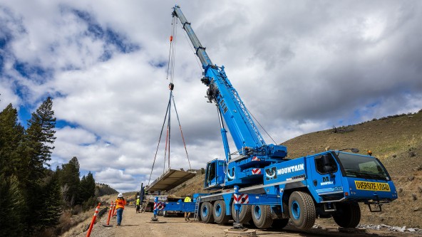 A Liebherr mobile crane lifts bridge components during demolition operations in Yellowstone, supporting controlled removal in a mountainous work environment. A Liebherr mobile crane lifts bridge components during demolition operations in Yellowstone, supporting controlled removal in a mountainous work environment.