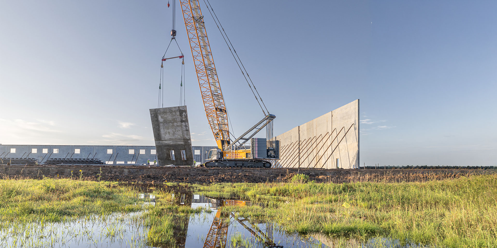 Heavy-duty crawler crane lifting a precast concrete wall panel at a construction site