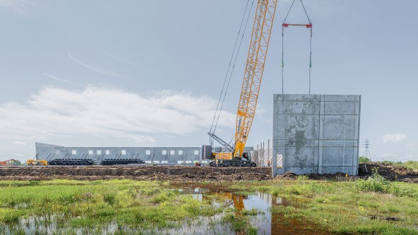 Wide-angle view of a Liebherr crawler crane installing a massive precast concrete wall panel